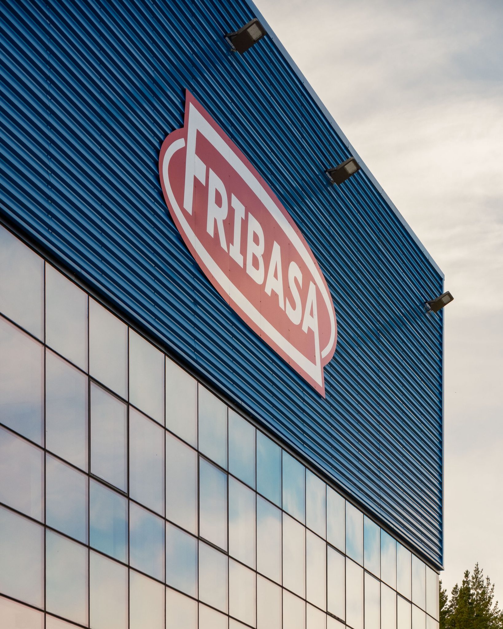 Detalle del logotipo de Fribasa sobre la fachada de chapa azul y el muro cortina